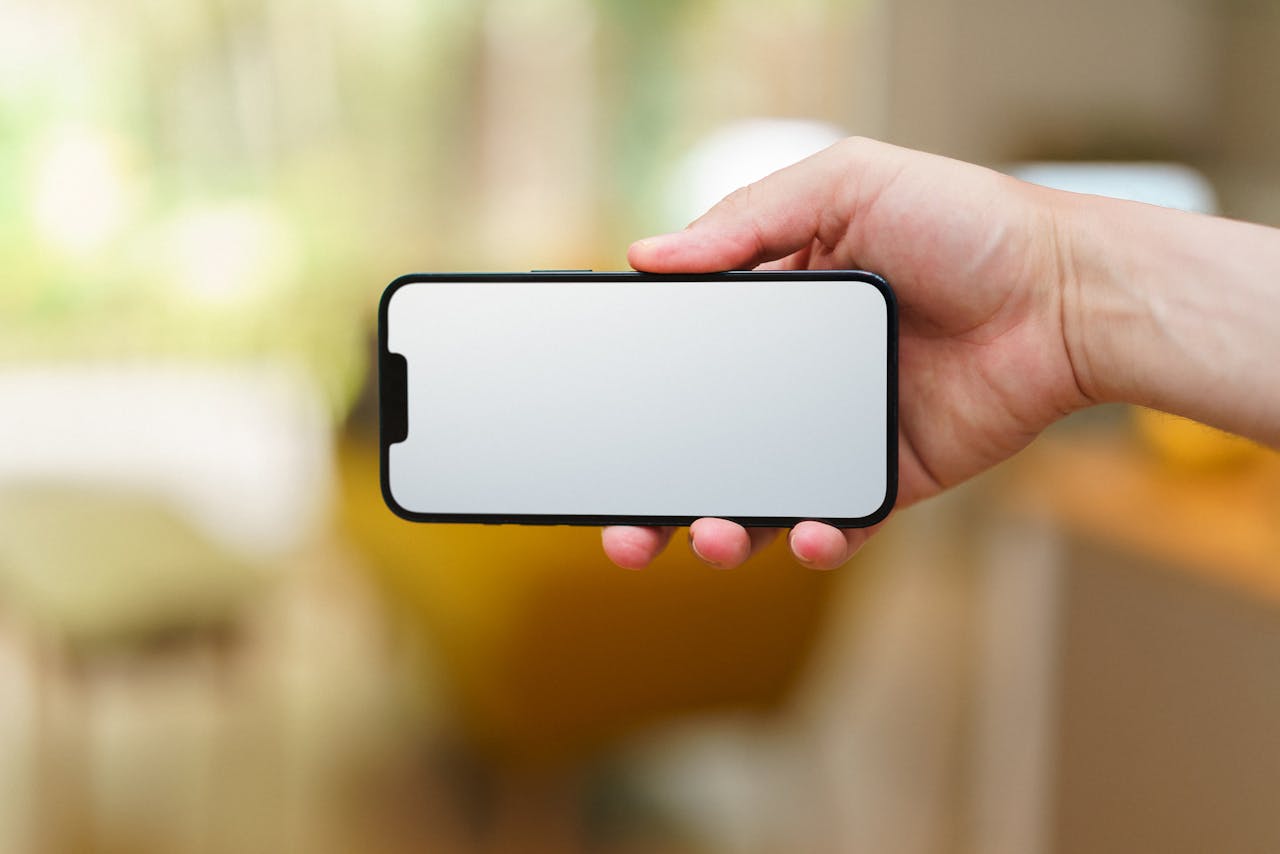 Close-up of a hand holding a smartphone with a blank screen, indoors.